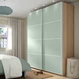 Modern bedroom with large light blue PAX wardrobe, wooden accents, and essentials like window curtains, a rug, and a laundry hamper.