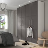 Minimalist bedroom with large grey PAX wardrobe. Tall, sleek, glossy, and mirrored with hanging shirt. Next to cozy bed and wooden chair.