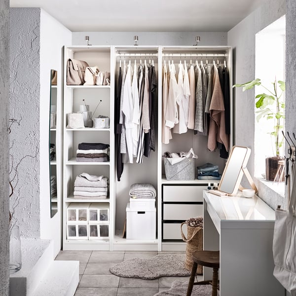 Modern walk-in closet with white PAX system, shelves, clothes, and vanity area.
