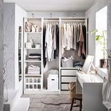 Modern walk-in closet with white PAX system, shelves, clothes, and vanity area.