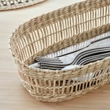 Wicker basket holding cutlery, natural and handwoven, sits on wooden table.