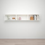 A minimalist white wall shelf with segmented compartments displaying decorative items and books.