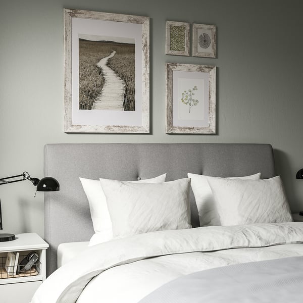 Cozy bedroom with gray headboard, rustic landscape print, black lamp, and white nightstand.
