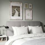 Cozy bedroom with gray headboard, rustic landscape print, black lamp, and white nightstand.