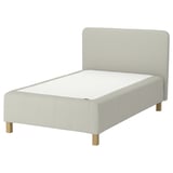 The RÅHOLMAR bed with a white mattress and beige upholstered headboard and base on light wooden legs.
