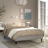 Neutral RÅHOLMAR bed with teddy pillow, flanked by lamps. Three art pieces above, large window with sheer curtains, stylish pendant light.