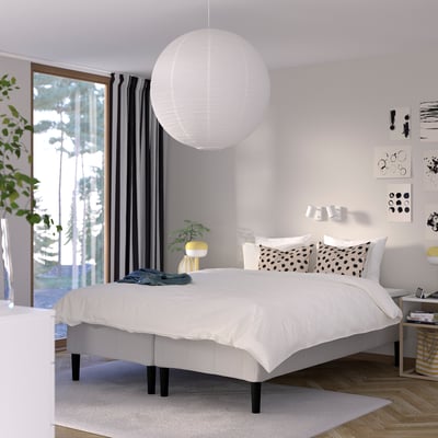Modern bedroom with white bed, large white pendant light, geometric pillows, and black curtains; large window.