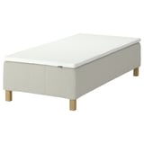 A white RÅHOLMAR bed base with a padded seat cushion on top, supported by wooden legs.