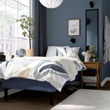 Modern blue bedroom: RÅHOLMAR bed, white linens, bedside table, plant, grey towels, large mirror.
