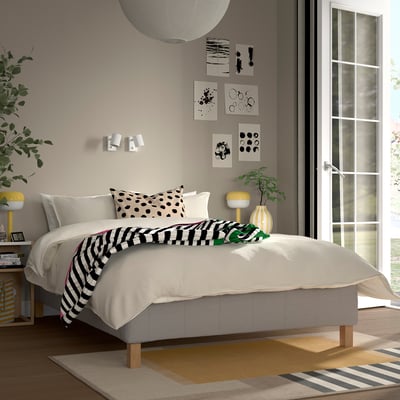 Modern bedroom with RÅHOLMAR bed, white linens, black-and-white pillows, striped throw, nightstand, yellow lamp, plant, large window.