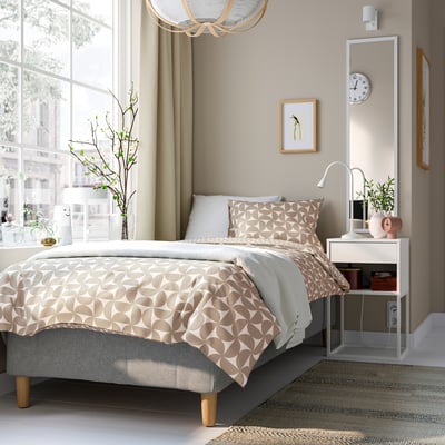 Modern bedroom with RÅHOLMAR bed, geometric print, large headboard, bedside table, chandelier, art, clock, plant, and large window.