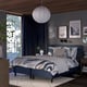 Modern bedroom with RÅHOLMAR bed, blue accents, pendant light, nature art, dark curtains, wooden floor, rug, nightstands.