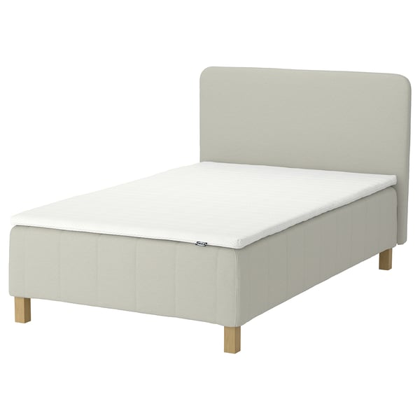 An IKEA RÅHOLMAR beige bed with five comfort zones for spine alignment, a soft headboard, and wooden legs.