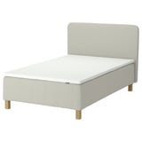 The RÅHOLMAR bed in light beige, featuring a memory foam mattress with five comfort zones, a padded headboard, and wooden legs.