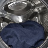 A blue fabric bed frame with a padded headboard and a removable, machine-washable cover inside a steel washing machine.