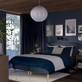 Modern dark blue bedroom with large bed, wooden furniture, and hanging lamp. Artwork and plants add decor.