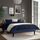 Gray-blue RENFJÄLLET bed, neat under art, white rug, wooden frame, colourful bedding.