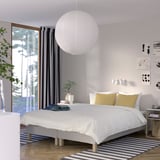 Modern bedroom with large bed, pendant lamp, artwork, and plant.