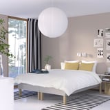 Minimalist bedroom with white bed, yellow pillows, large light, dark curtains, striped rug, art walls.