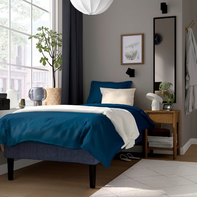 Modern bedroom with RENFJÄLLET bed, blue/white colours, grey wall, bedside table, window, plant.