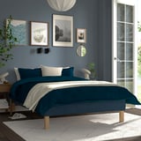 Minimalist bedroom with RENFJÄLLET bed, blue linens, and white pillows. Blue walls, artwork, sunlight streaming through.