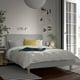 Modern grey bed with grid duvet, yellow pillow, nightstand plant, artwork above.