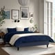 Modern bedroom with navy bed, white pillows, wooden bedside table, framed art and large window.