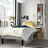 Modern bedroom with white RENFJÄLLET bed, striped rug, and minimalist decor. Large mirror enhances spacious feel.