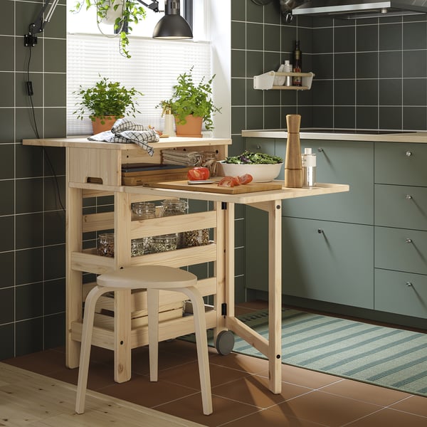 Modern kitchen with light wood RESARÖ drop-leaf table, natural finish, potted plants, and green cabinets.