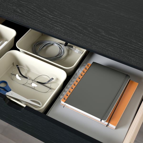 Desk drawer with organized trays: glasses, charging cable, notebook, scissors, and pen.