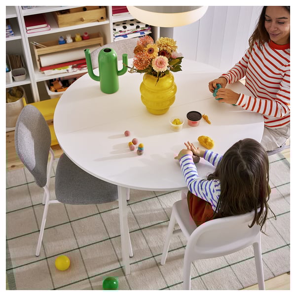 Adult and child play with toys at round table. Table has vase, cactus can, and rug with green checks.