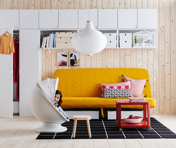 Yellow sofa, colorful pillows, modern room, white lamp, unique chair, striped shirt, black rug.
