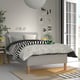 Modern bedroom with RISHÖJDEN bed. Grey bed, black & white bedding, striped rug. Mattress has 7 comfort zones. Bed is large, fits under tall windows.