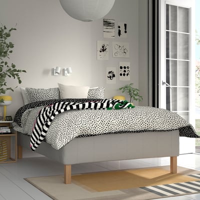 Modern bedroom with RISHÖJDEN bed; grey, dotted sheets, black stripes; large, cosy, white pillows; wooden legs; near window.