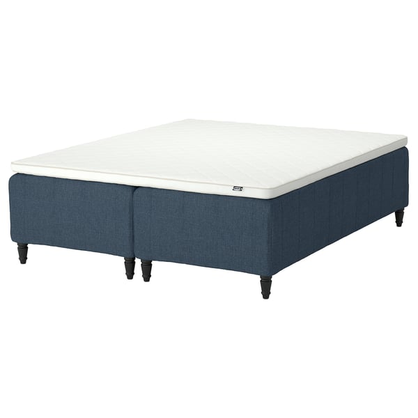 A grey-blue upholstered bed with a white mattress, featuring a low footboard with turned legs.