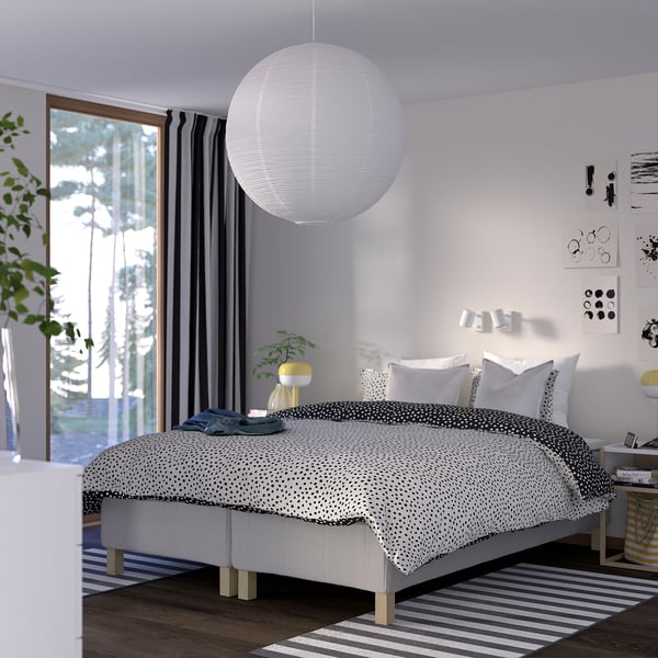 Modern bedroom with white bed, blackout curtains, pendant lamp, nightstand, yellow lamp, striped rug, plant.