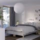 Modern bedroom with white bed, blackout curtains, pendant lamp, nightstand, yellow lamp, striped rug, plant.
