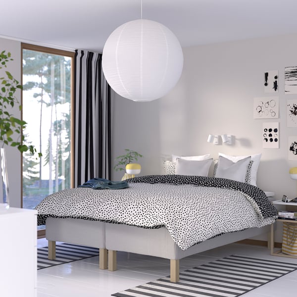 Modern bedroom with RISHÖJDEN bed, white base, dotted bedding, large lamp, striped rug, gray curtains, art gallery, clean feel.