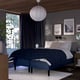 Modern cosy bedroom with blue bed, dark wood, white lamp, large window, and bedside table.