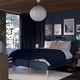 Blue bedroom with RISHÖJDEN bed, dark blue walls, white lamp, wood accents, art, nightstands, window, plant.