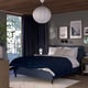 Modern bedroom with blue RISHÖJDEN bed, dark grey headboard, blue curtains, geometric bed cover, white pillows, and decorative elements.