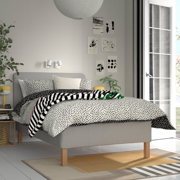 Modern grey RISHÖJDEN bed, plush headboard, pillows, throws, large window, rug, nightstands with lamps, wall art.