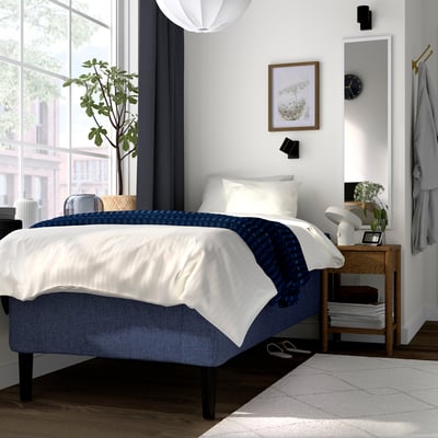 Modern bedroom with RISHÖJDEN bed: white & blue, wooden frame, pocket springs, plant, bedside table, natural light.