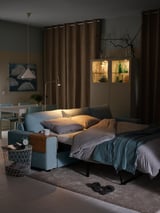 Cozy dim living room with light blue sofa bed, wooden tray table, and curio cabinet.