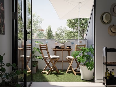 Modern balcony with green RUNNEN grass, wooden chairs, and plants. Large window and white umbrella.