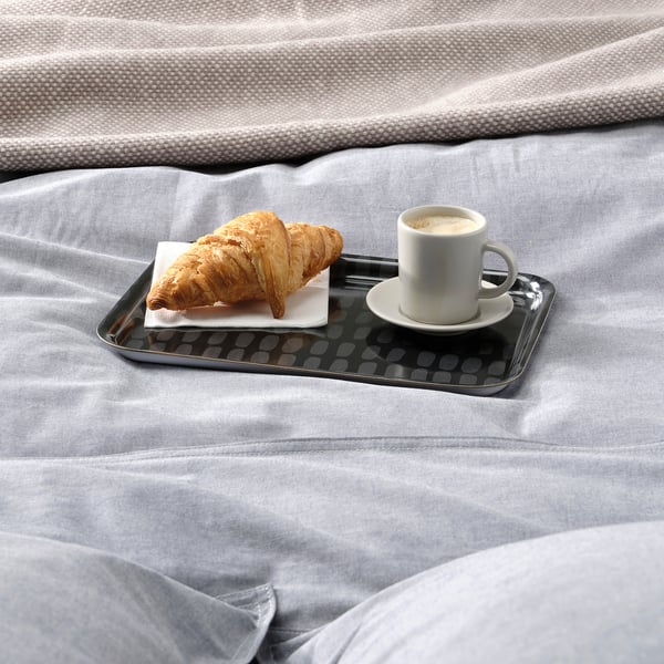 Tray with croissant and coffee sits on bed for breakfast in bed.