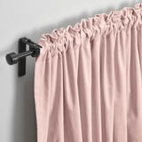 Blush pink velvet curtains hang on modern black rod, gently pleated, filtering light, offering privacy and warmth.