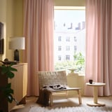 Bright room with pale pink SANELA curtains, a wicker chair, and minimalist decor, offering a cozy, stylish atmosphere.