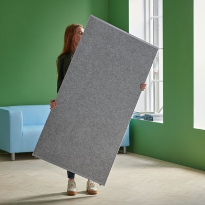 A person holding a large gray panel room divider in a green room.