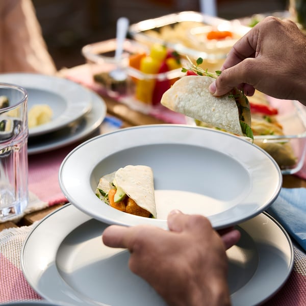 Hand holding green-grey plate with wrap. Casual meal setting, simple and sturdy design, ideal for gatherings and easy to carry.